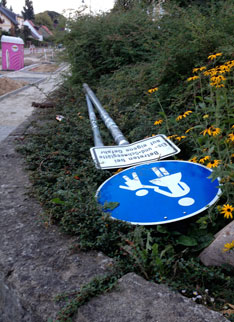 Foto von einem Straßenschild, welches auf Anpflanzung geworfen wurde, ist zu sehen.